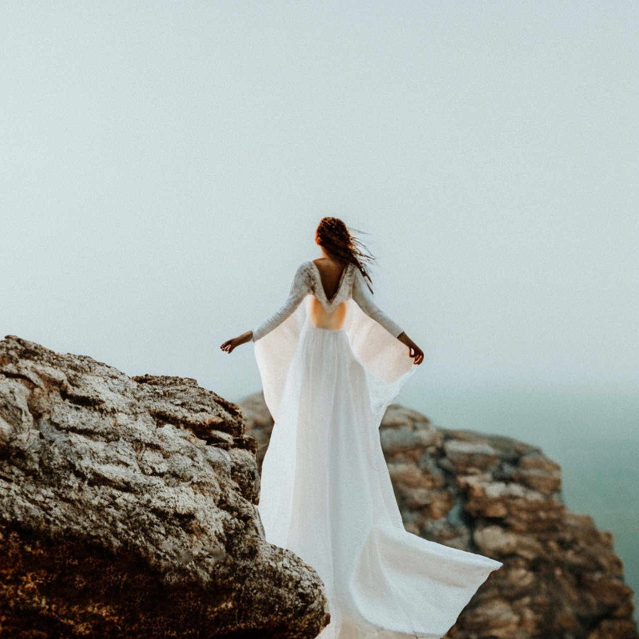 Woman in Flowing White Dress on Rocky Cliff