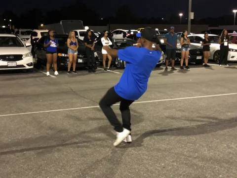 Man Dancing in Parking Lot at Night with Onlookers
