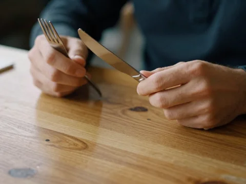 Person Holding Fork and Knife at Wooden Table
