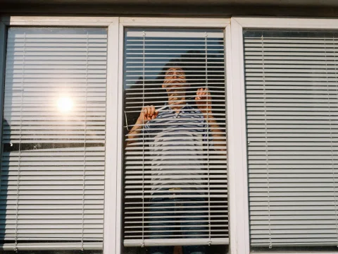 Person Opening Window Blinds on a Sunny Day