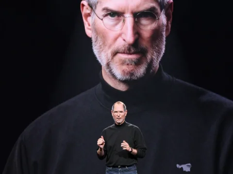 Steve Jobs Presenting on Stage with Large Portrait Background