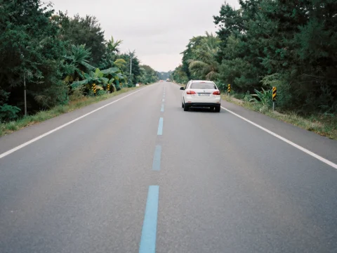 White Car Driving on a Quiet Road Surrounded by Greenery
