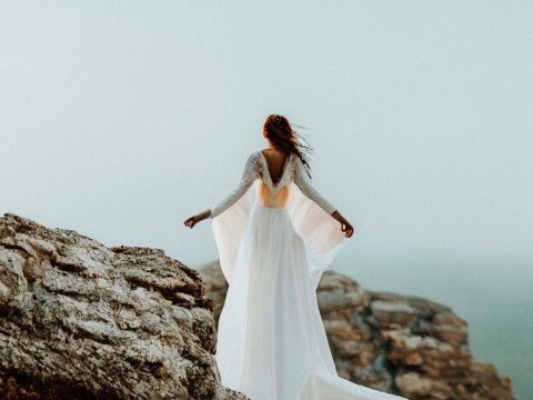 Woman in Flowing White Dress on Rocky Cliff